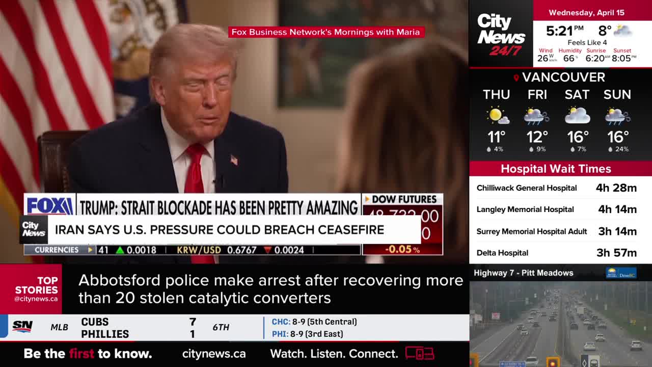 A man in a suit and red tie speaks on a screen, with news tickers scrolling below. To the right, the Vancouver weather forecast and hospital wait times are displayed. A man in a suit and red tie speaks on a screen, with news tickers scrolling below. To the right, the Vancouver weather forecast and hospital wait times are displayed.