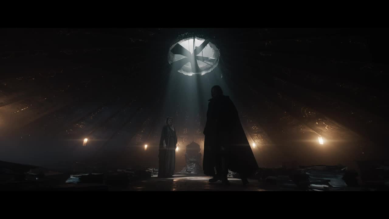A shaft of light pierces the darkness from above, illuminating two figures standing in a cavernous space. One, cloaked and imposing, faces the other, who seems to be awaiting a verdict.
