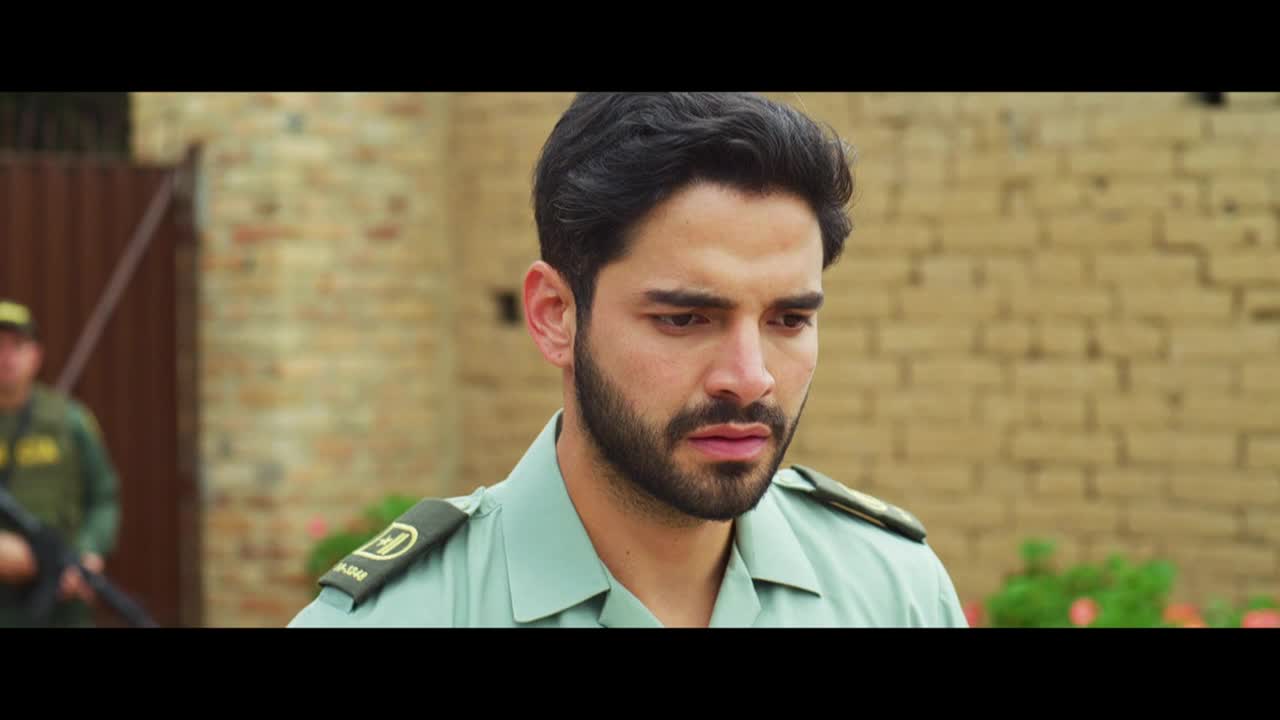 The officer in the light green uniform stares down, his expression etched with concern. Behind him, another officer stands guard, his rifle held at the ready.
