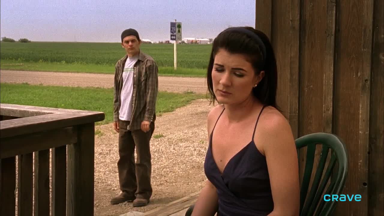 A young woman sits, looking down, while a man stands a few feet away, his gaze fixed on her. The scene feels heavy, like a moment of quiet tension from a Canadian Crave 2 show.
