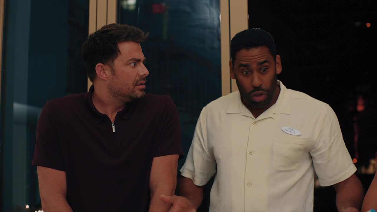 The man in the maroon shirt glances to the side, his expression a mix of surprise and concern. Beside him, the other man's mouth is open in shock, his eyes wide.
