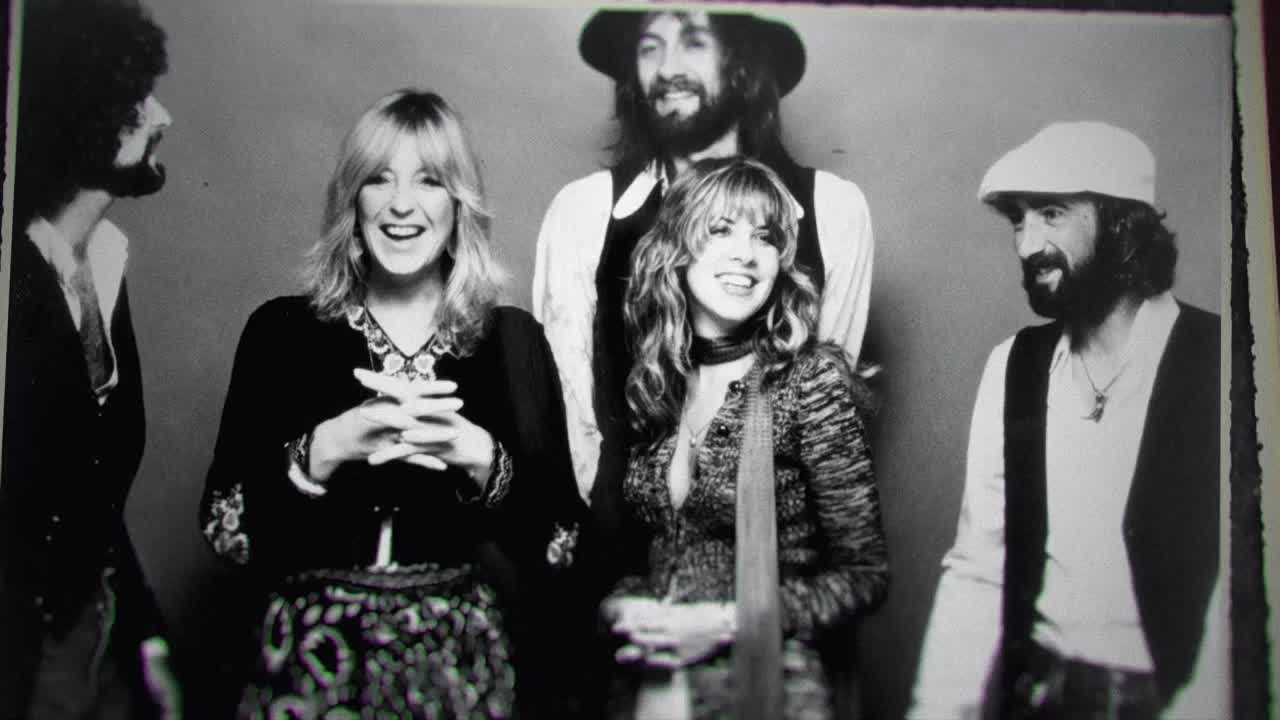 The band members are posed together, smiling, with their hands clasped or at their sides. The two women are in the middle, flanked by the men in a classic black and white photo.

