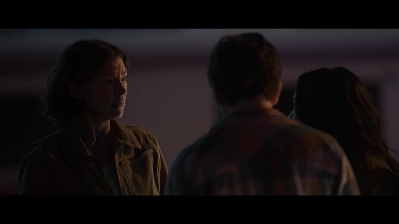 A woman, lit from the side, looks intently at the man facing her. Her face is etched with concern, while the man's back is turned, obscuring his expression.
