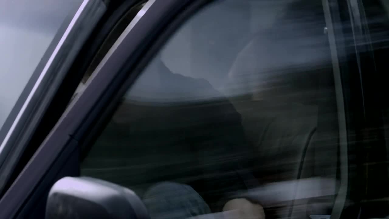 A car speeds past, the window reflecting a blurred landscape. Inside, a person's silhouette is visible, their face obscured by the motion.
