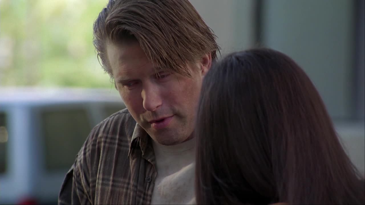 The man in the plaid shirt is looking down, speaking softly to someone just out of view. His expression is concerned, and he seems to be leaning in close.
