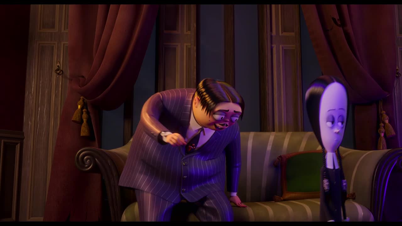 Gomez, in a pinstripe suit, gestures emphatically while leaning toward the sofa. Wednesday Addams stands nearby, her expression characteristically unimpressed.
