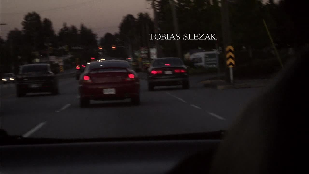 Three cars are driving down a dark street, the red one in the middle is clearly visible. The name Tobias Slezak is superimposed on the scene.
