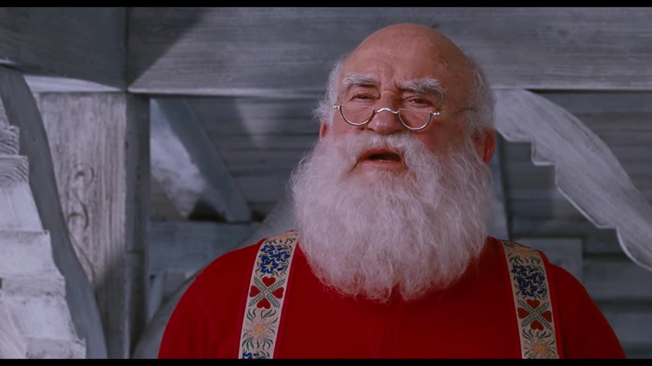 Santa Claus, in his red suit and suspenders, looks up with a slightly surprised expression. Behind him, a white veil or curtain billows in the air, likely a scene from a movie on Crave 4.
