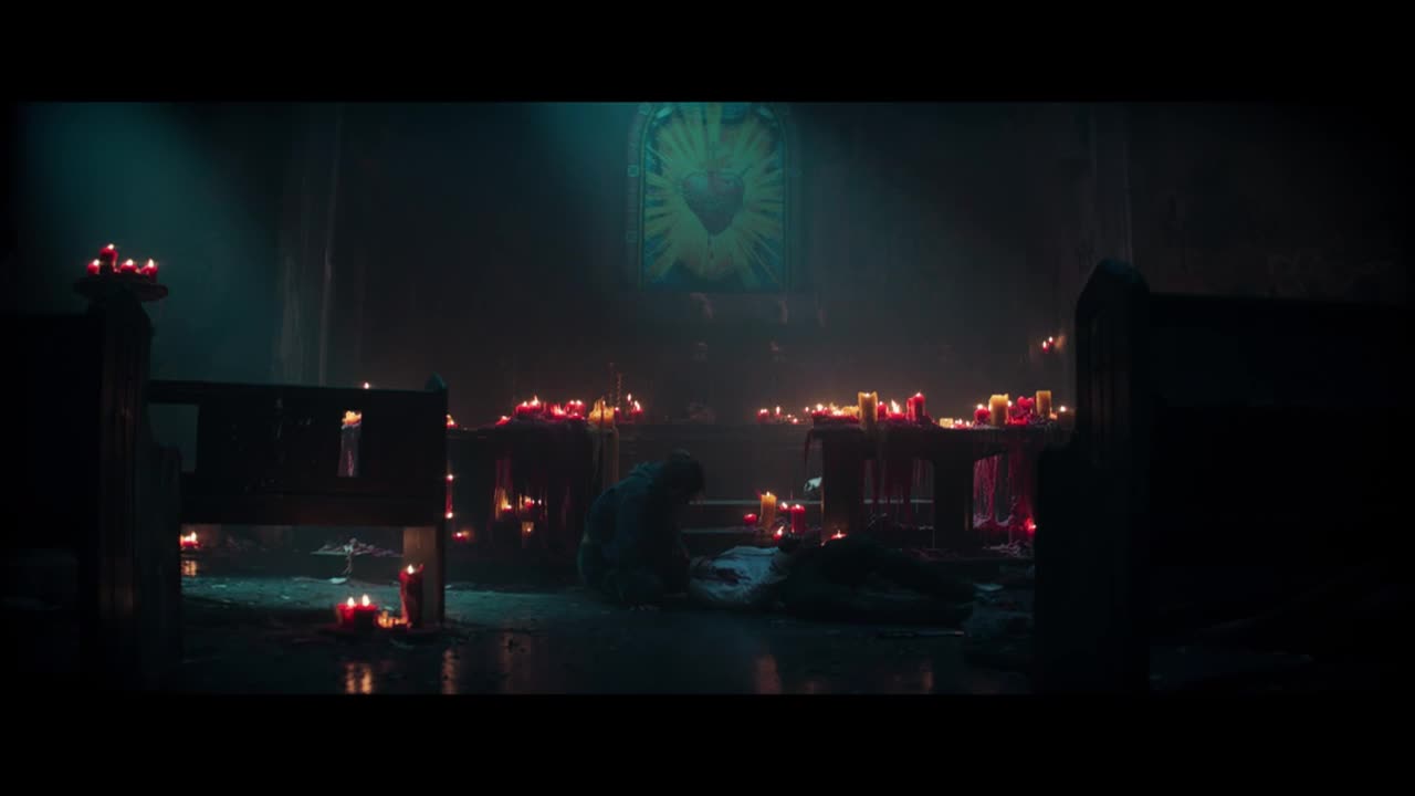 A figure kneels on the floor, illuminated by the flickering candlelight. The scene is set in a dimly lit church, with rows of candles burning on the altar and pews.
