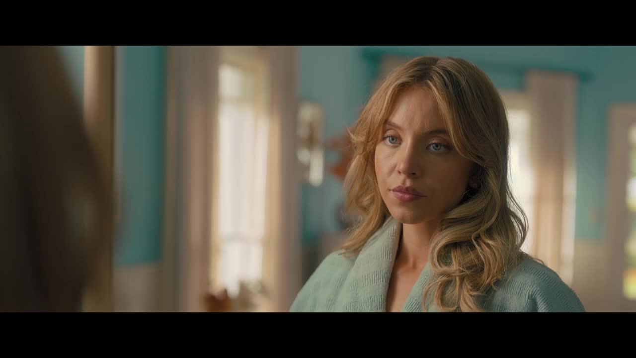 She's in a light green robe, looking directly at someone out of frame. Her blonde hair is curled, and the background suggests a bright, airy room.
