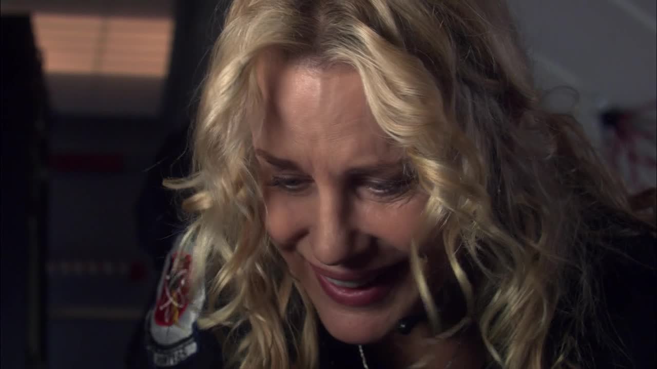 Her face is tilted down, her eyes glistening, and her lips are slightly parted in a small, sad smile. The blonde hair is a tangled, soft curtain around her face.

