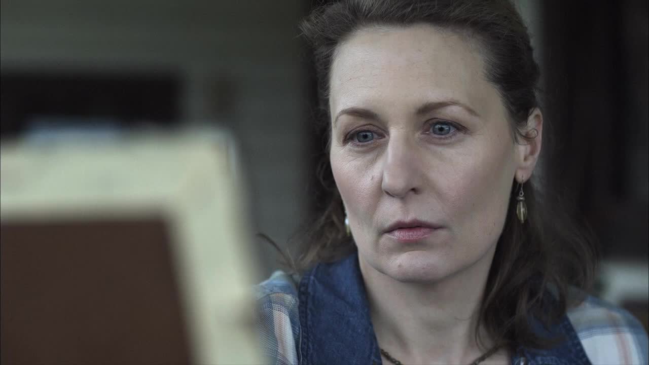 The woman's gaze is fixed, her eyes narrowed as she looks at something just out of view. A soft light catches the lines on her face, emphasizing her serious expression.
