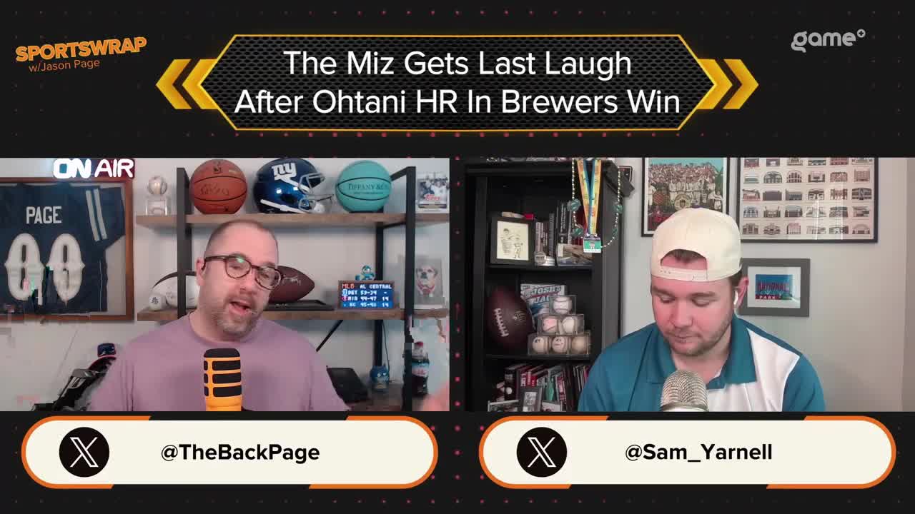 Two men sit at a desk, each with a microphone, discussing a Brewers win on Game+. The man on the left gestures animatedly, while the other listens intently, wearing a baseball cap.
