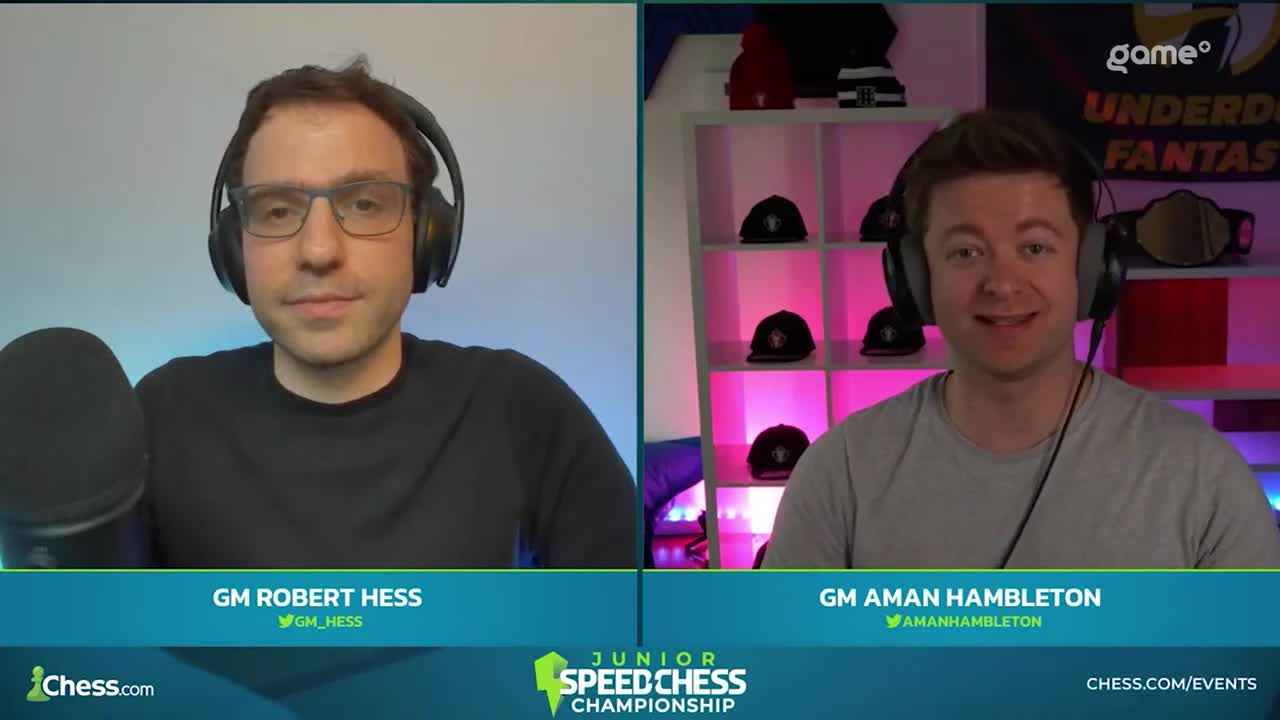 Two chess grandmasters, Robert Hess and Aman Hambleton, are on camera, each in their own split screen. Hess, wearing glasses and a headset, looks directly at the camera, while Hambleton smiles, with a rack of hats visible behind him.
