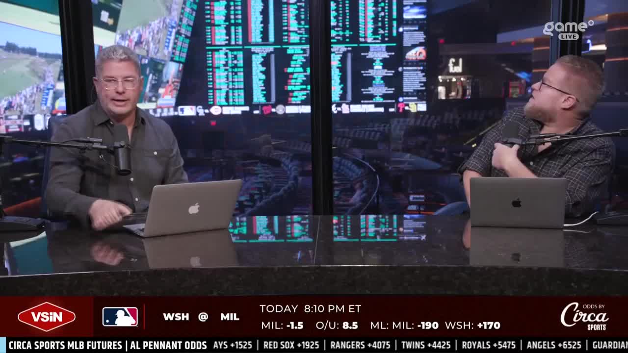 Two men sit behind a desk, each with a laptop and microphone, discussing sports. Behind them, a large screen displays betting odds and a golf tournament, all under the Game+ banner.
