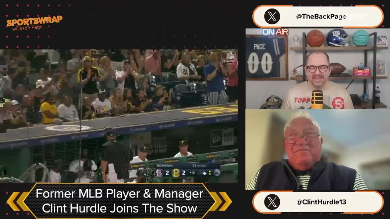The crowd is clapping, and the game is on the screen, but the focus is on the two men in the boxes, one of them a former MLB player, Clint Hurdle, joining the show. The host, Jason Page, is smiling, while Hurdle is looking at the camera.
