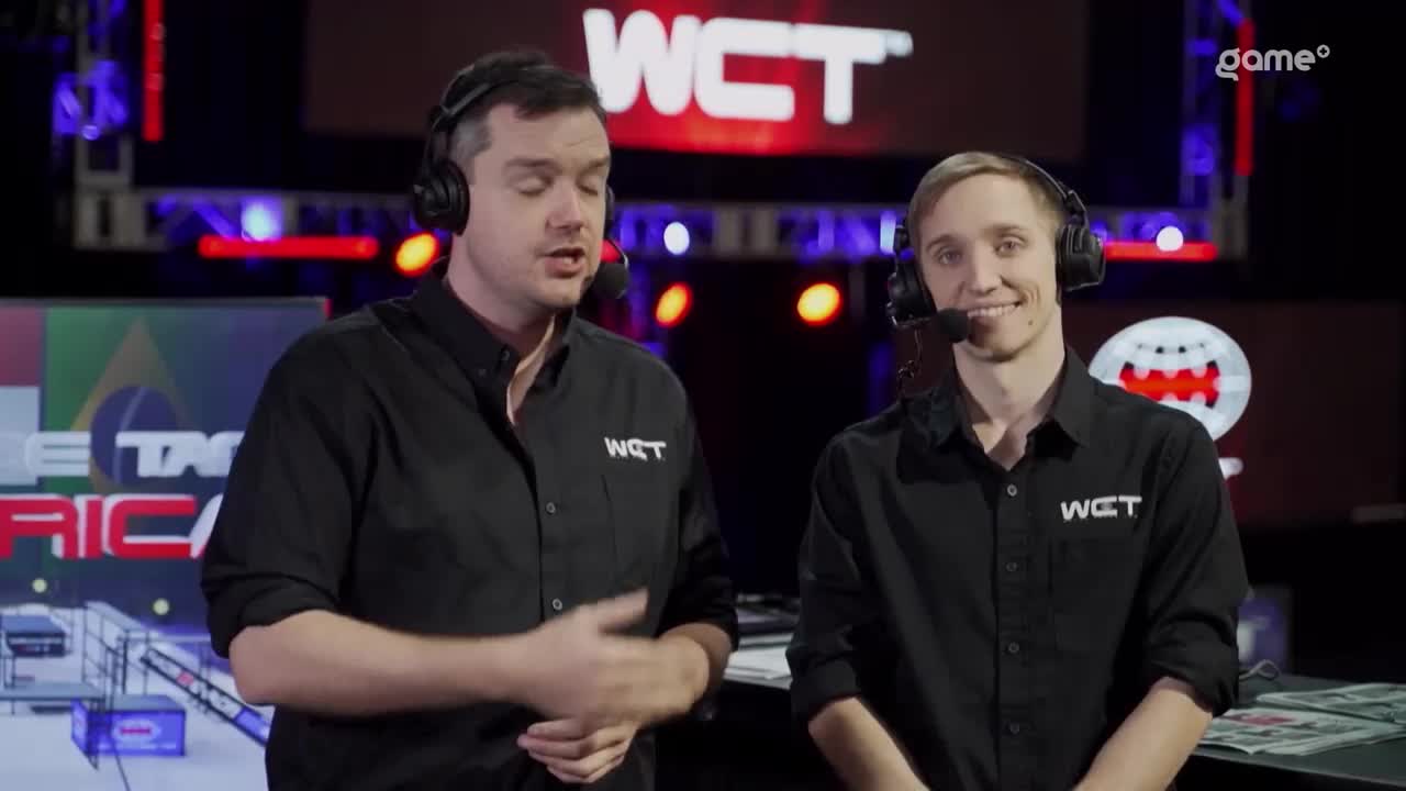 Two men in black WCT shirts are speaking into microphones, likely broadcasting for the Canadian Game+ audience. The background is a brightly lit stage with a WCT logo and a stylized map.
