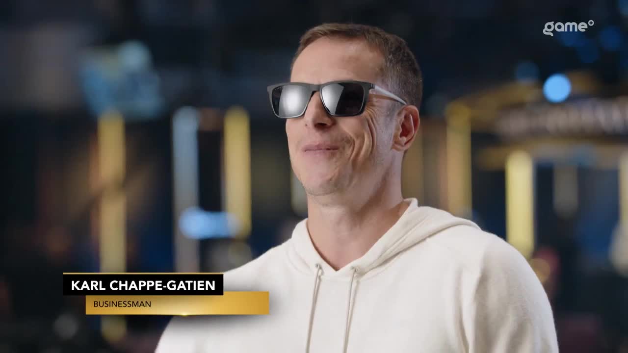 A man in sunglasses smiles, his name and occupation displayed on a lower third graphic. The Game+ logo is visible in the background.
