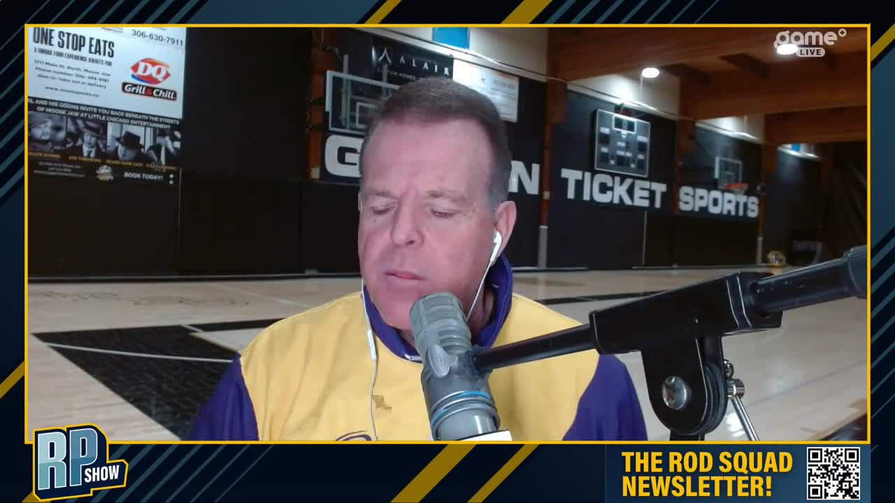 A man in a yellow and purple jacket speaks into a microphone, likely on a Game+ broadcast. Behind him, a basketball court and a sign for "N. Ticket Sports" are visible.
