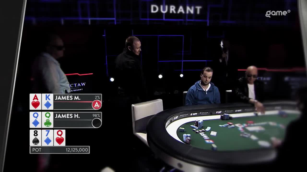 A poker game is underway, with the cards showing on the screen. The players are focused on the table, with one man standing behind a seated player.
