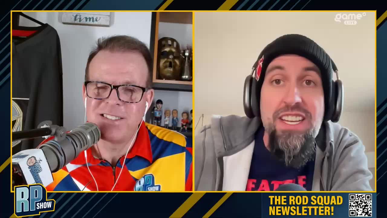 The man on the left, wearing a colourful shirt, speaks into a microphone. Across from him, a man with a beard and beanie listens intently. The man on the left, wearing a colourful shirt, speaks into a microphone. Across from him, a man with a beard and beanie listens intently.