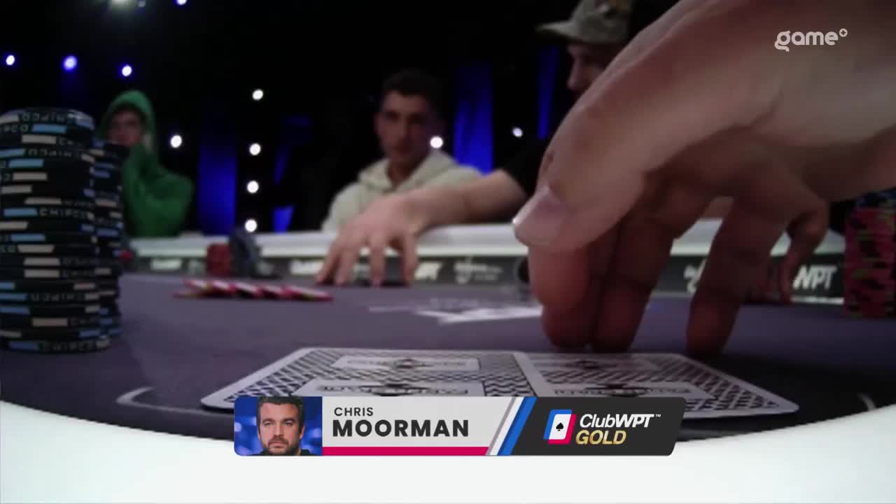 Chris Moorman's hand hovers over his cards as he considers his next move. The Game+ broadcast captures the intense focus at the poker table.
