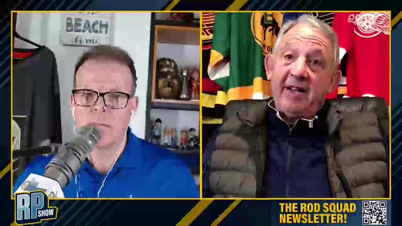 The screen splits between two men, one with glasses and a blue shirt, the other in a puffer vest. Behind the man in the vest, hockey jerseys in green and red hang on the wall.