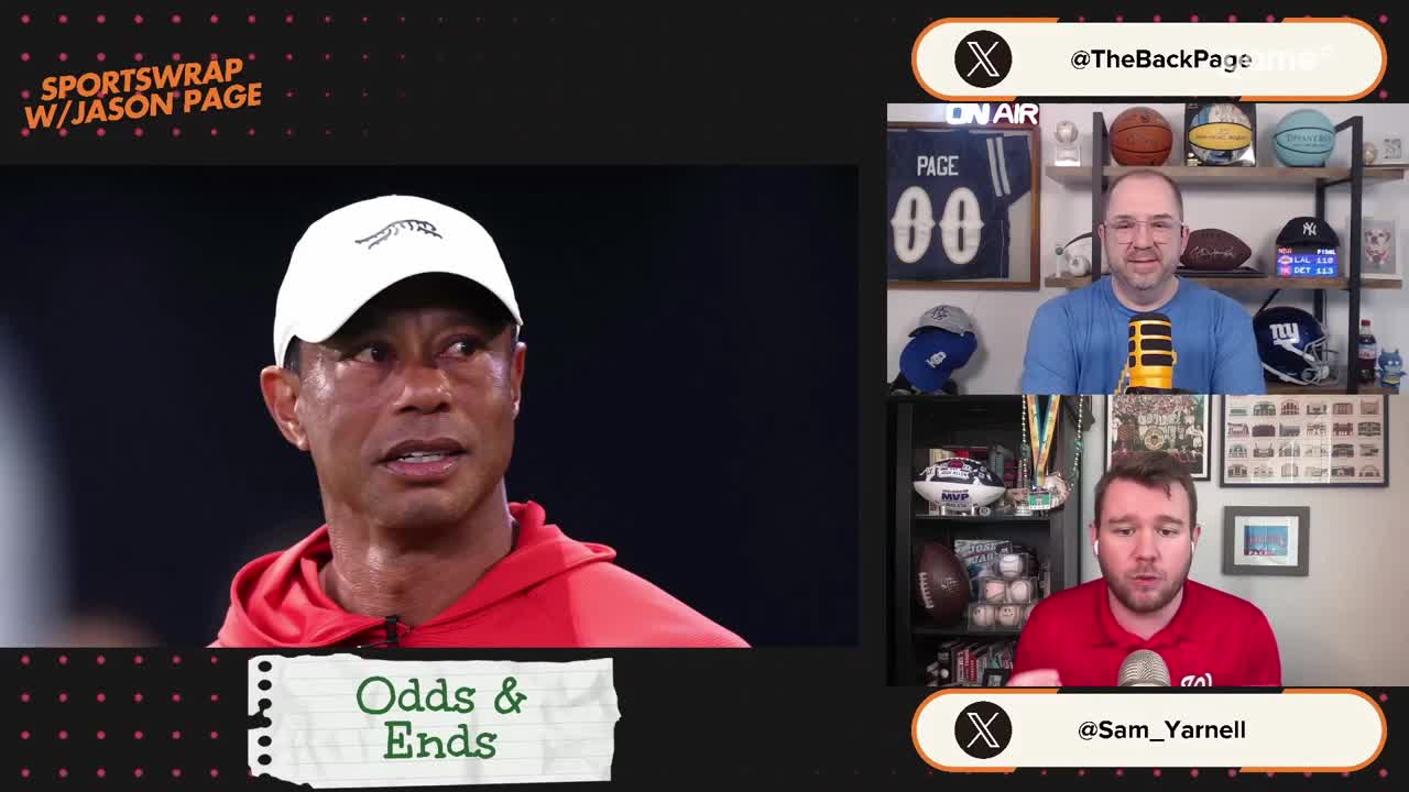 Tiger Woods, wearing a red hoodie and white cap, looks off to the side. Two men are on screen, one in a blue shirt and the other in a red shirt, speaking into microphones.