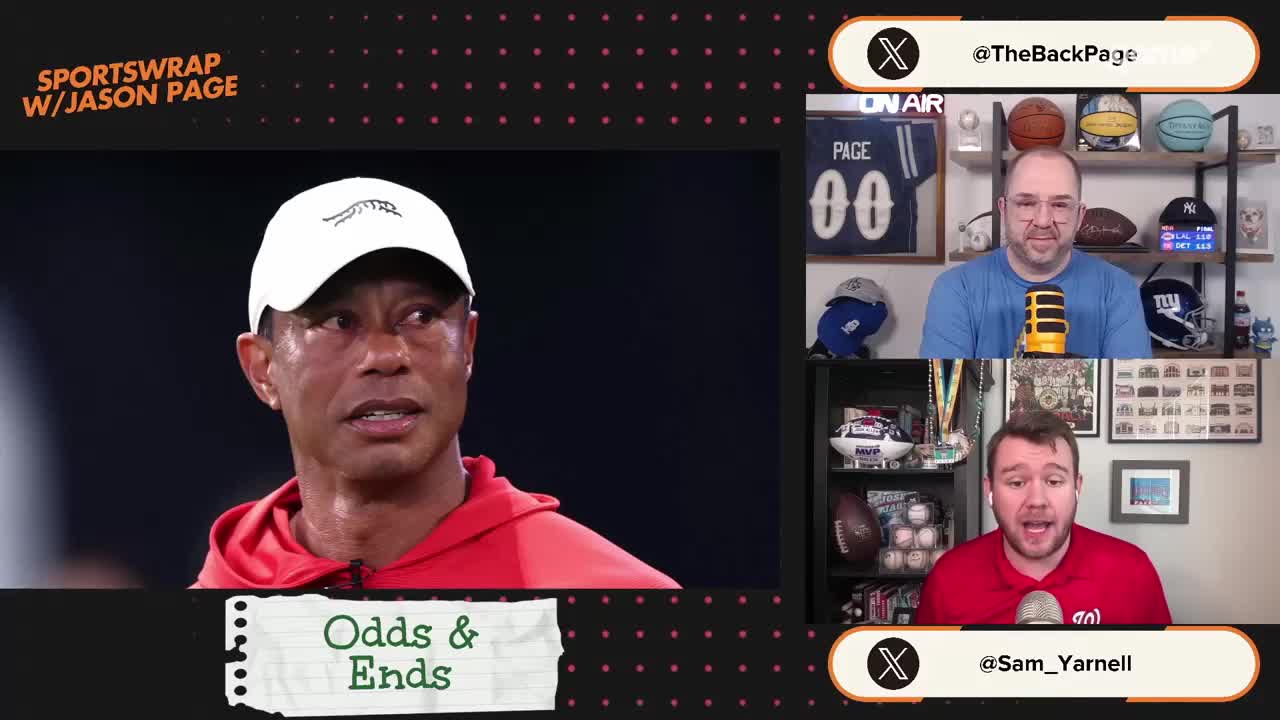 Tiger Woods, wearing a red hoodie and a white cap, looks intently off to the side. Two men are on screen, one in a blue shirt and the other in a red one, both speaking into microphones.