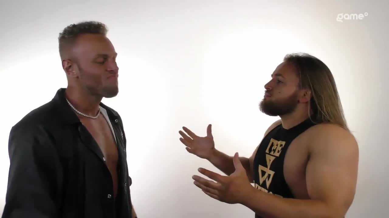 Two men stand facing each other, one with his mouth pursed and the other gesturing with open hands. The Game+ logo is visible in the corner, suggesting this is part of a broadcast.