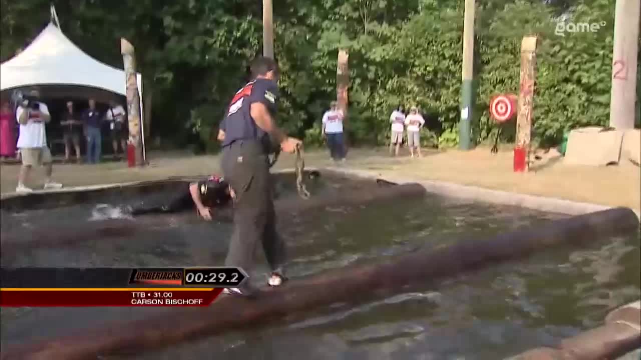 A competitor is struggling in the water as another person, likely a handler from Game+, pulls on a rope. The scoreboard shows Carson Bischoff's time is 00:29.2. A competitor is struggling in the water as another person, likely a handler from Game+, pulls on a rope. The scoreboard shows Carson Bischoff's time is 00:29.2.