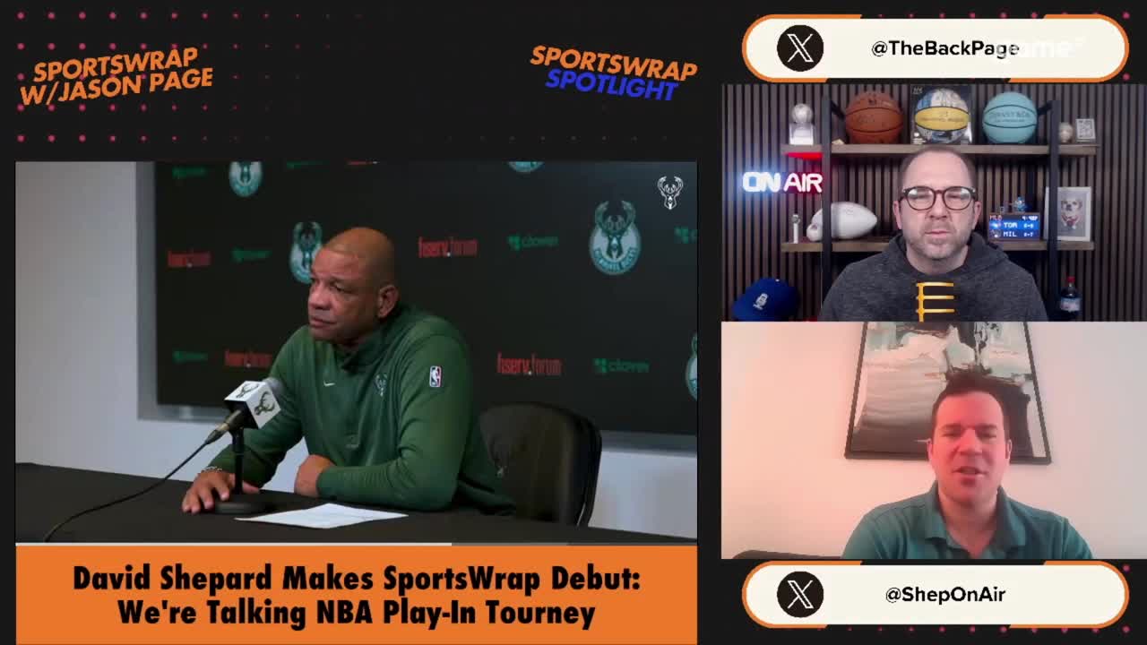 A man in a green jacket sits at a table, speaking into a microphone. Above him, two other men are on screen, one wearing glasses and a grey hoodie, the other in a teal shirt.