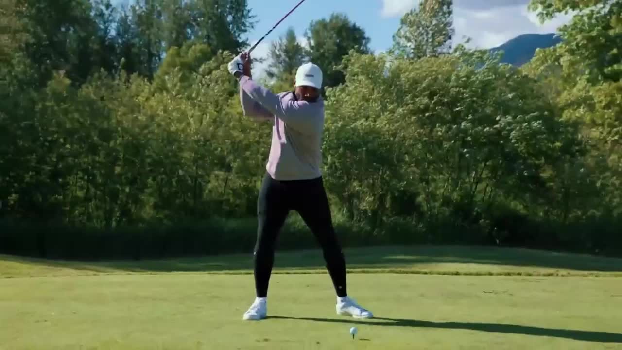 The golfer is mid-swing, the club arcing high above their head. A small white ball sits on the tee, waiting for impact.