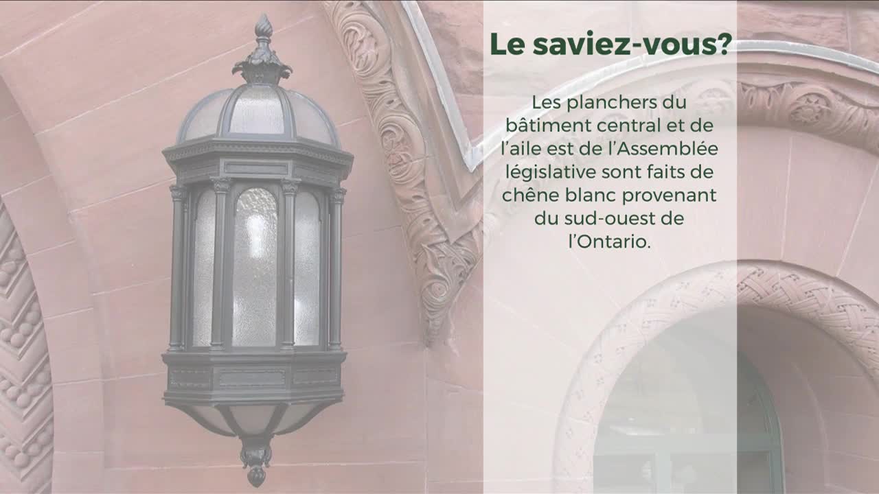 A decorative, ornate lamp hangs on a weathered stone wall, likely part of the Legislative Assembly in Ontario. The text next to it informs me the floors of the building are made of white oak.
