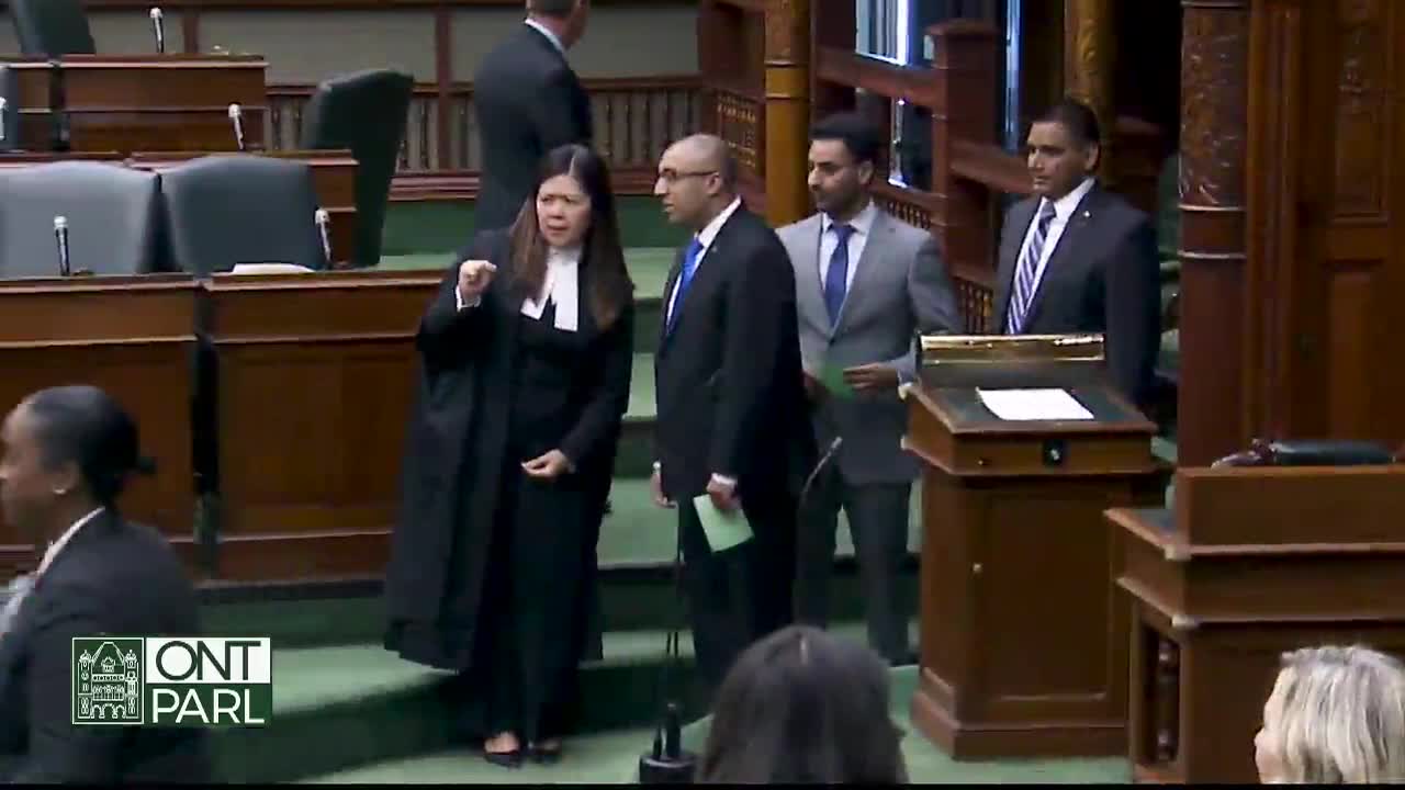 A woman in a black robe gestures emphatically, speaking to a group of men in suits. The scene unfolds within the Legislative Assembly of Ontario, with the "ONT PARL" logo visible.
