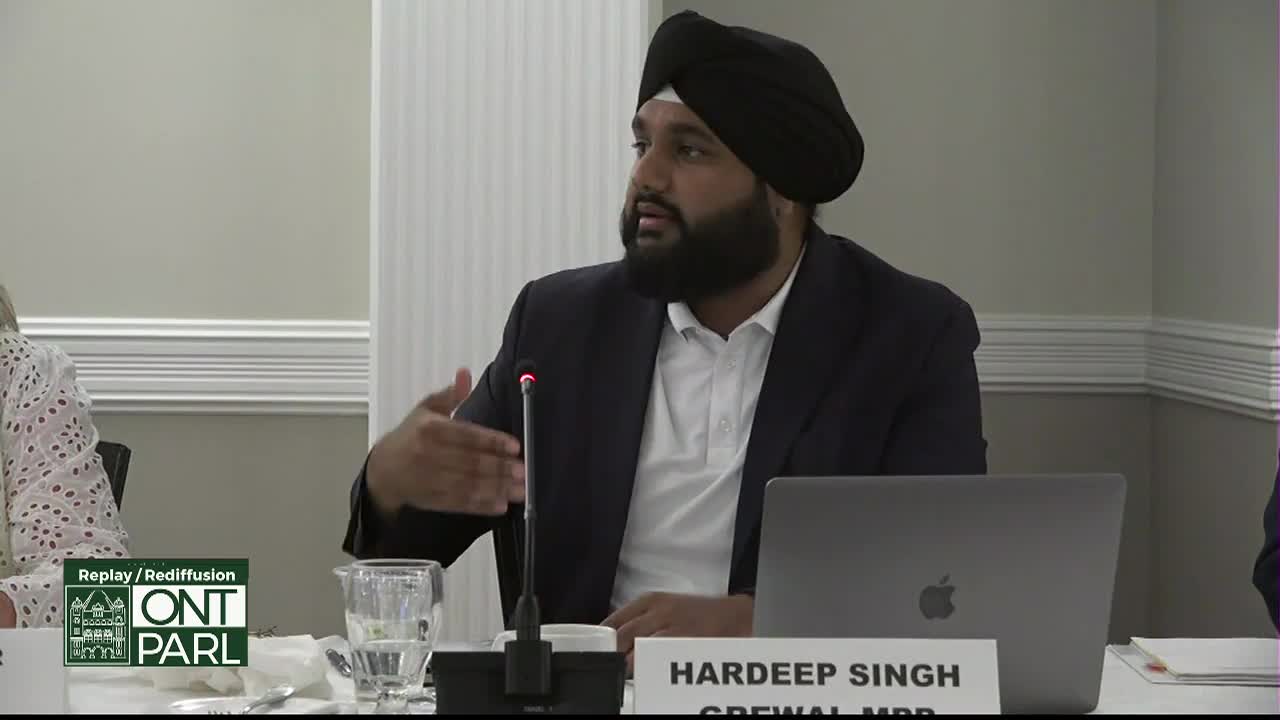 At the Legislative Assembly of Ontario, Hardeep Singh, Grewal, MPP, gestures with his right hand as he speaks. A microphone sits in front of him, and a laptop is open on the table.
