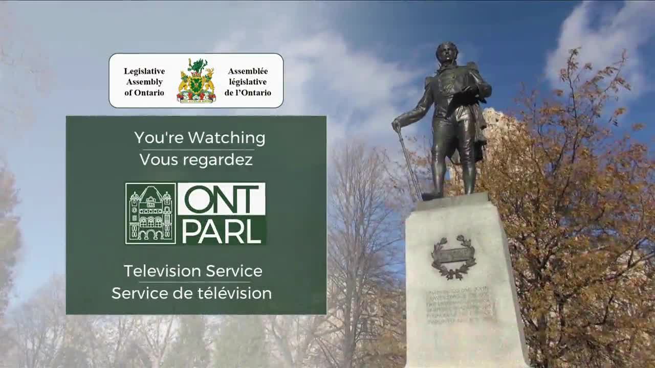 A bronze statue of a man stands tall, overlooking a park. Beside it, the Legislative Assembly of Ontario's television service logo indicates what's being broadcast.
