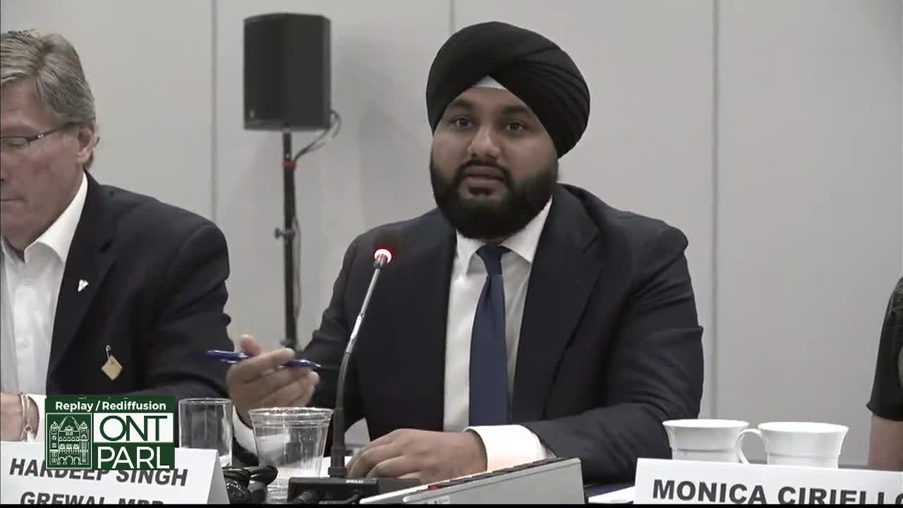 A man in a turban, speaking into a microphone, gestures with a pen while seated at a table. The Legislative Assembly of Ontario logo is visible in the corner.
