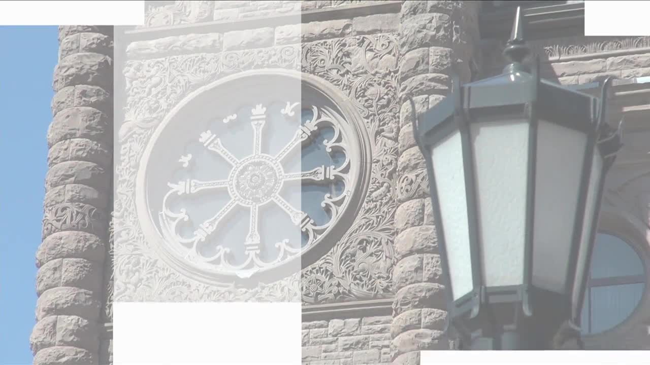 The ornate stonework of the Legislative Assembly of Ontario rises against a clear blue sky. A decorative lamp post hangs nearby, its glass panels reflecting the light.
