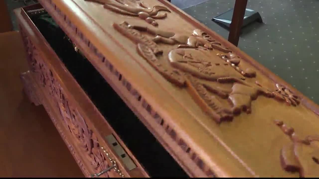 The lid of a carved wooden casket is slightly ajar, revealing a glimpse of the dark interior. Intricate figures are etched into the wood, catching the light.
