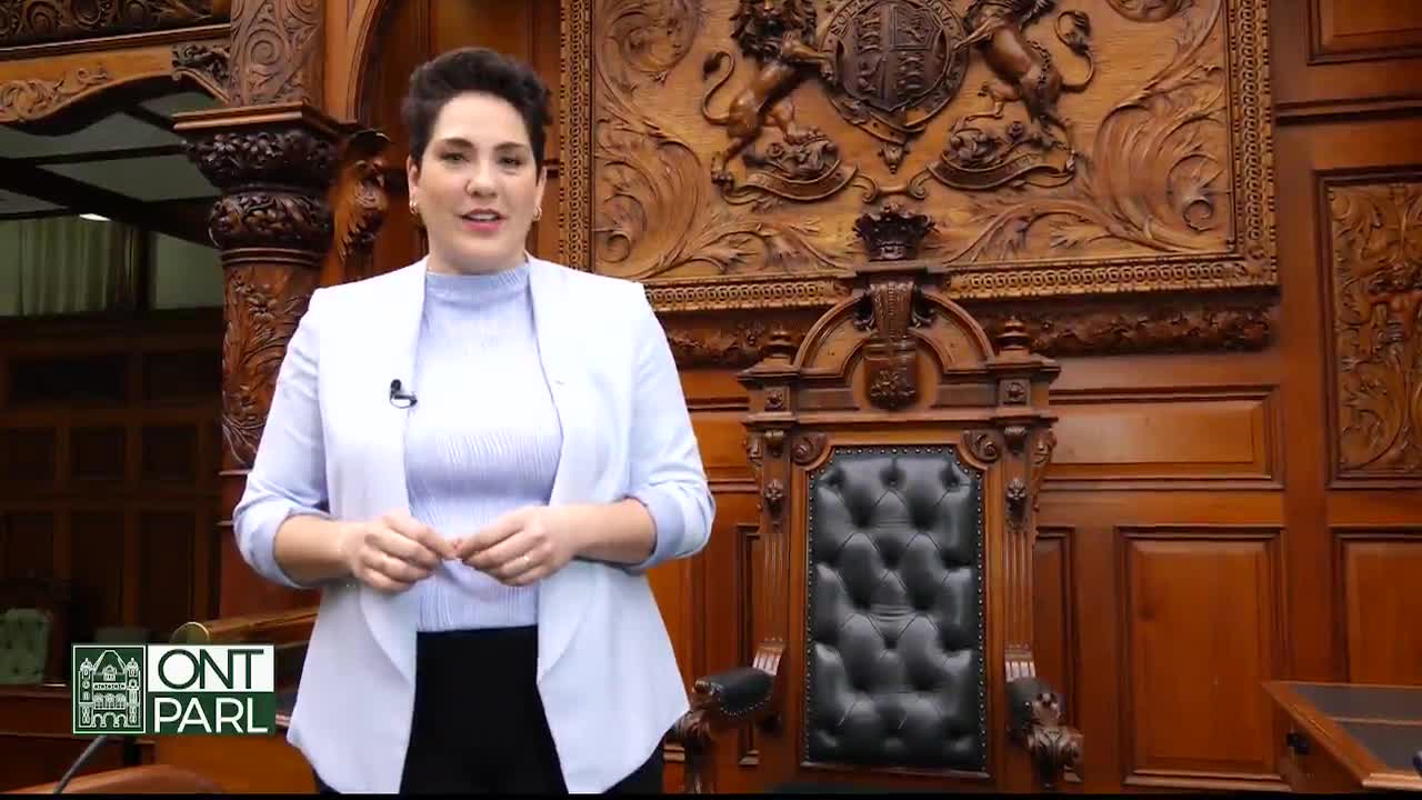 A woman in a light blazer stands in front of a large, ornate wooden chair, likely in the Legislative Assembly of Ontario. The background features intricate carvings and the seal of Canada, suggesting a formal setting.
