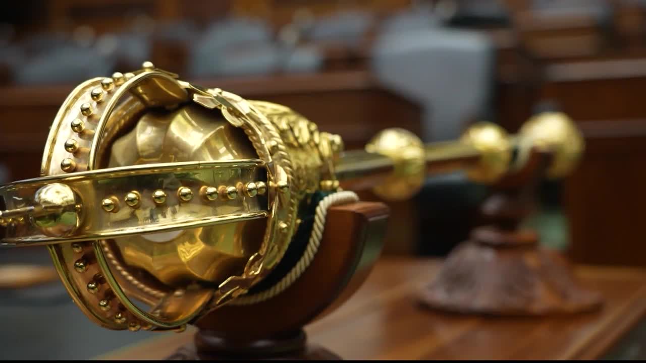 The ceremonial mace, a symbol of the Legislative Assembly of Ontario, rests on its wooden stand. Its ornate golden details gleam in the light.
