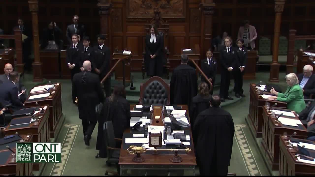 In the Ontario Legislative Assembly, people in black robes and suits are walking around the speaker's chair. Some students in uniforms stand on the stairs, watching the proceedings.
