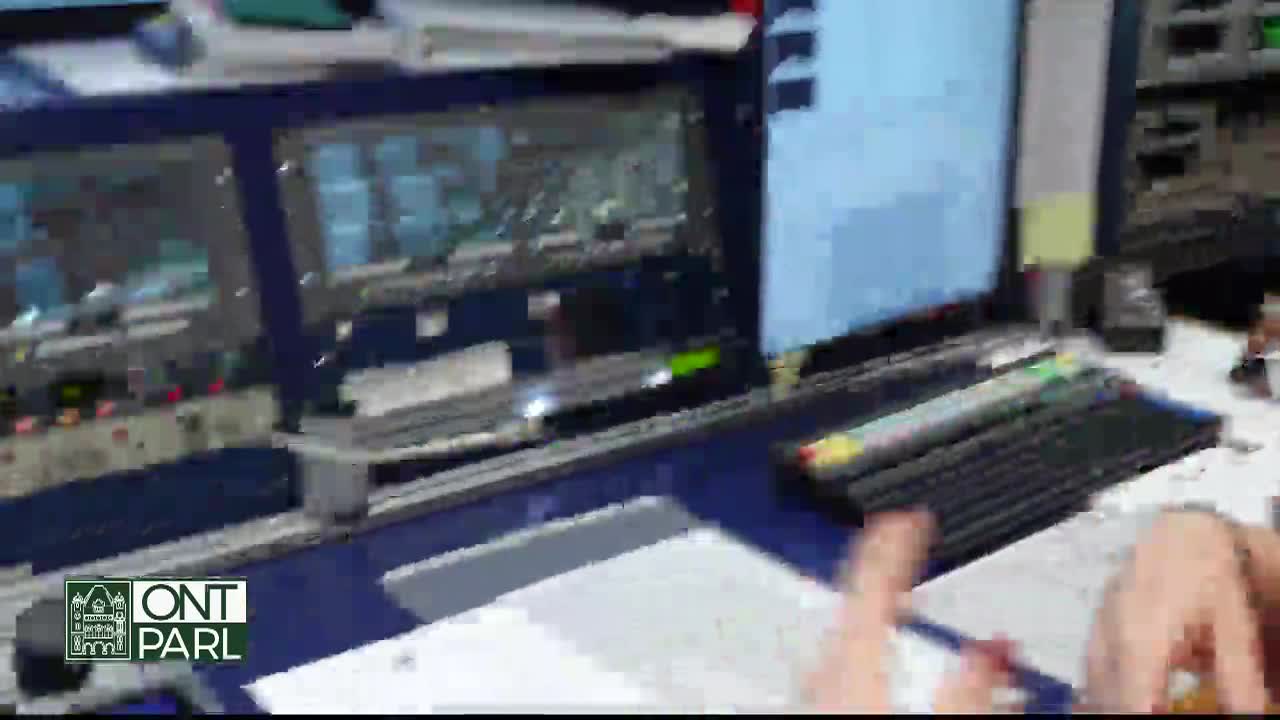 A control room at the Legislative Assembly of Ontario is in operation, with monitors displaying information and a person's hands working at a desk. The "ONT PARL" logo is visible, indicating the broadcast's source.
