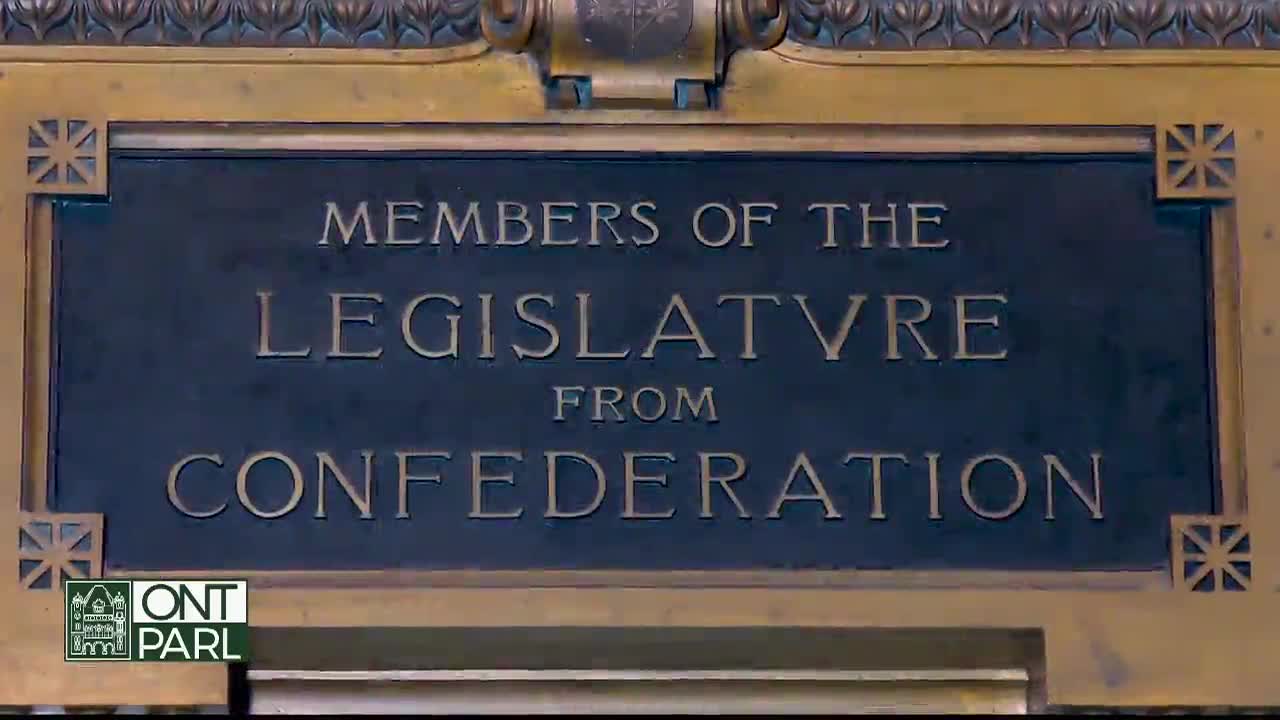A bronze plaque, inscribed with the words "Members of the Legislature from Confederation," is affixed to a wall. The logo of Ontario Parliament is visible in the corner.
