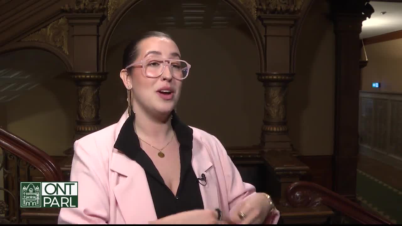 A woman in a pink blazer speaks, her hands gesturing as she stands on a staircase. The logo for Ontario Parliament, "ONT PARL," is visible in the corner.
