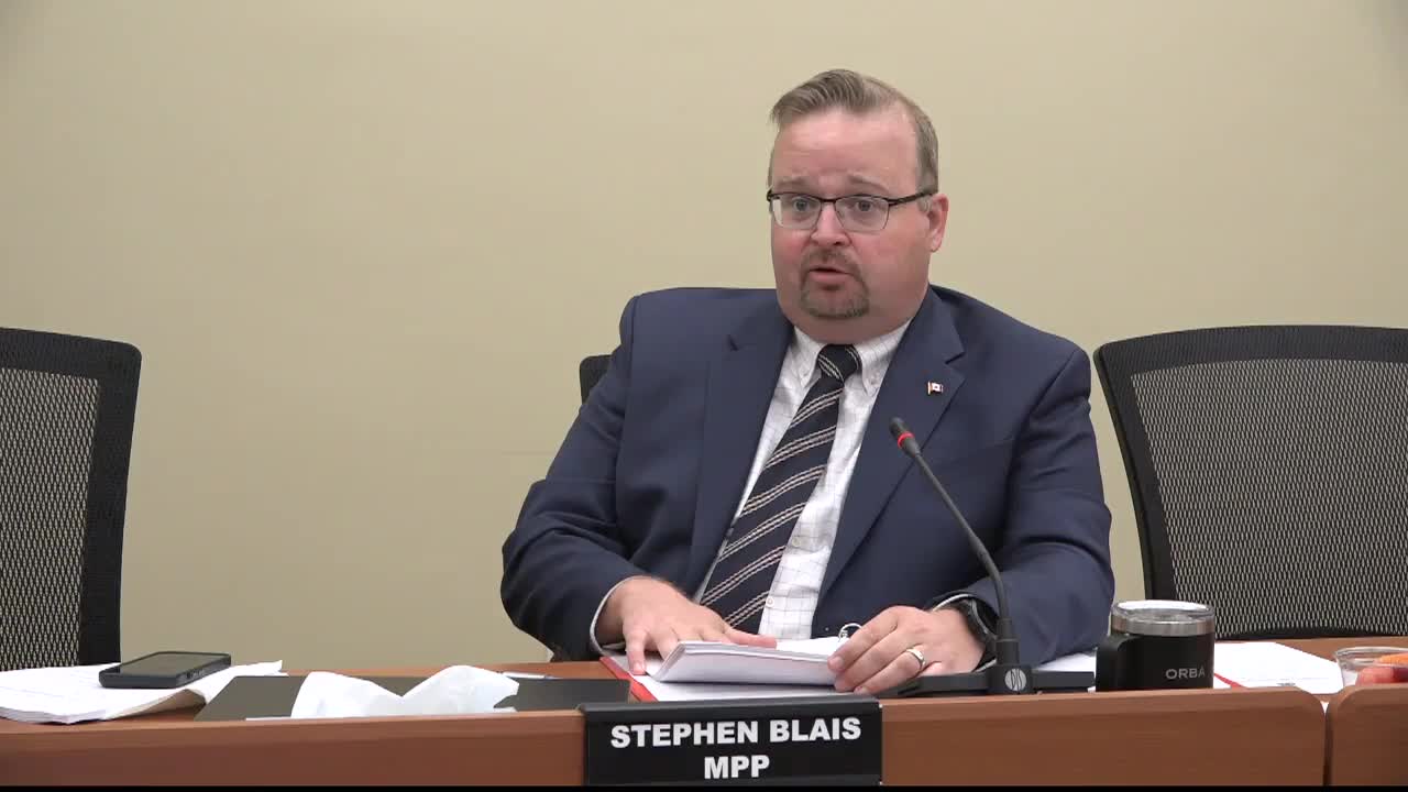 Stephen Blais, MPP for the Legislative Assembly of Ontario, is seated at a table, speaking into a microphone. He's holding a stack of papers and appears to be making a point.
