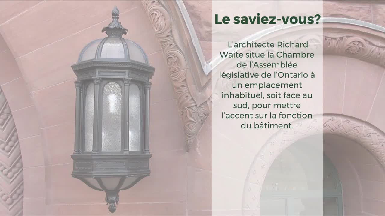 A decorative, ornate lamp hangs on the exterior of a building, likely part of the Legislative Assembly of Ontario. The lamp's glass panels are frosted, and the surrounding stonework has intricate carvings.
