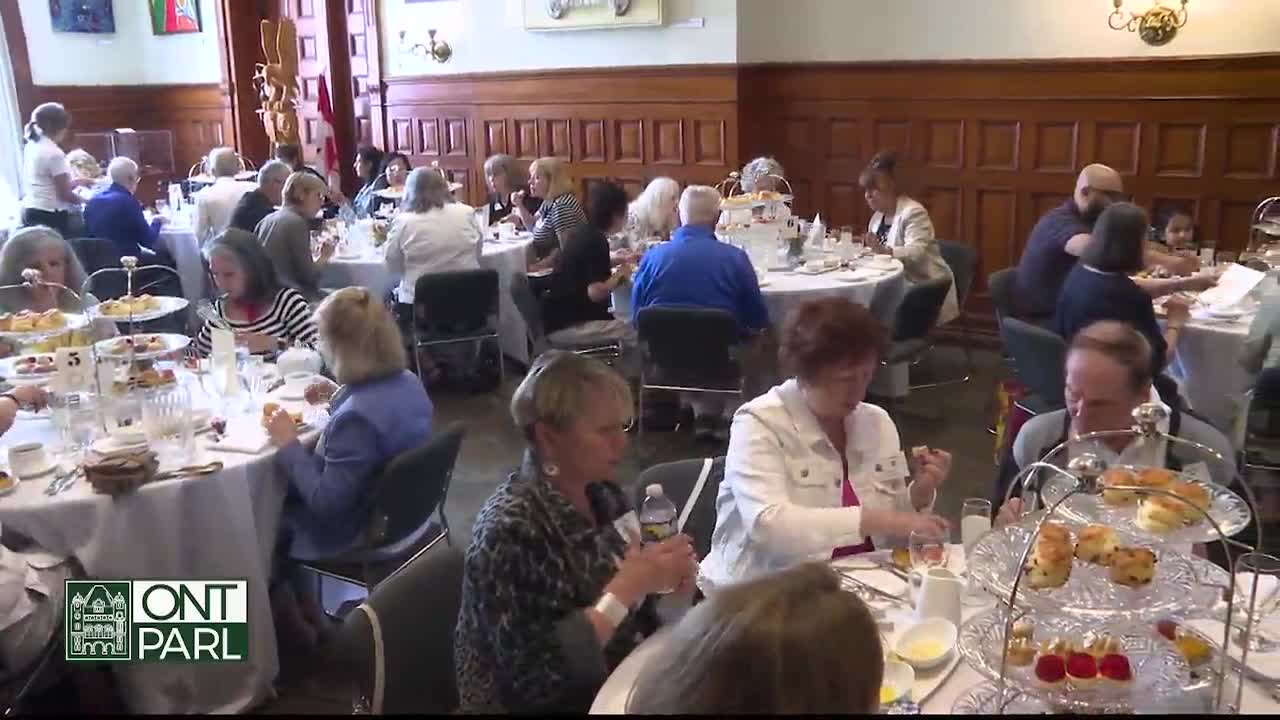 People are seated at round tables, enjoying afternoon tea in what appears to be a formal setting. The room is filled with the murmur of conversation and the clinking of silverware.
