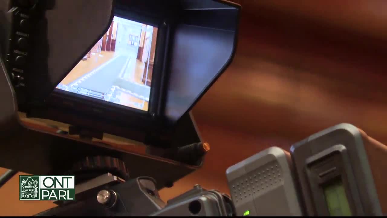 The camera's screen shows a long hallway, likely within the Legislative Assembly of Ontario. The equipment is set up, ready to capture the scene unfolding on the other side of the lens.
